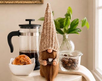 May include: A decorative gnome figurine with a tall, ribbed beige knit hat and a long brown beard, holding a miniature white coffee mug. The gnome is positioned next to a glass French press, a white bowl containing a pastry, and a glass bowl of nuts.