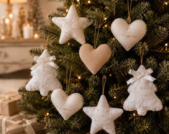 May include: A collection of hanging Christmas tree ornaments in white and beige. The set includes fabric stars, hearts, and tree shapes, some featuring delicate lace patterns, small white bows, and tiny pearl-like bead accents.