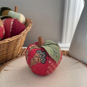 Single red patchwork fabric apple featuring coordinating floral cotton prints and a cinnamon stick stem.