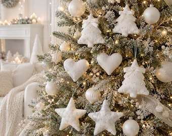 May include: A flocked Christmas tree decorated with white ornaments including fabric hearts, stars, and Christmas tree shapes adorned with small bows and beads. The tree is illuminated with warm white string lights and features various round baubles.