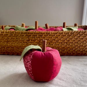 Close-up of a handmade red patchwork fabric apple with embroidered felt leaves and a natural cinnamon stick stem.