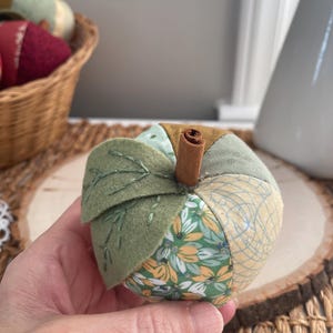 Close-up of a green patchwork fabric apple showing its handmade construction, felt leaves and cinnamon stem.
