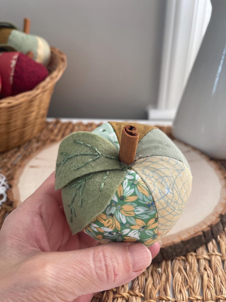 Close-up of a green patchwork fabric apple showing its handmade construction, felt leaves and cinnamon stem.