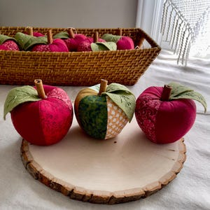 Red and green handmade fabric apples styled by a window with a wicker basket and farmhouse decor.
