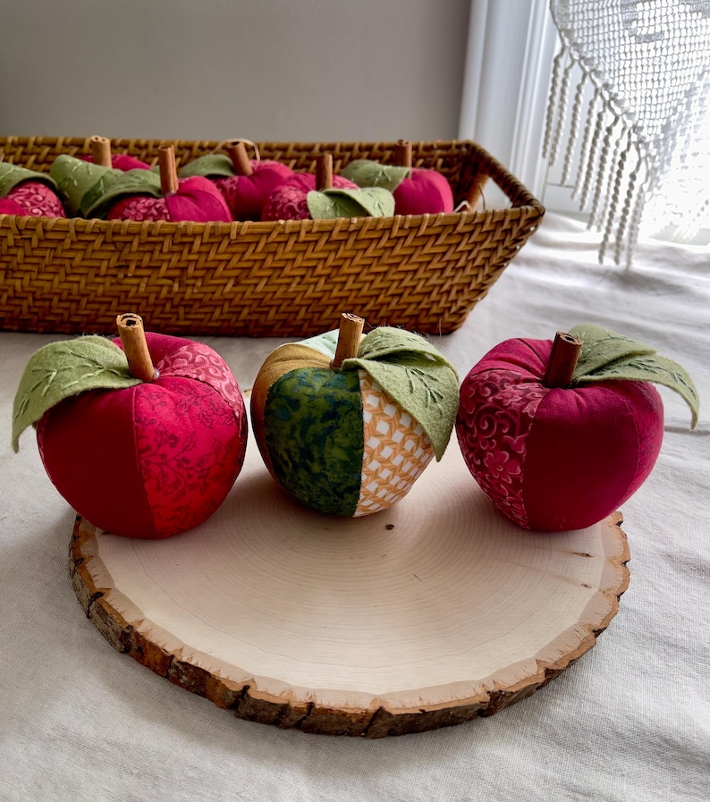 Red and green handmade fabric apples styled by a window with a wicker basket and farmhouse decor.