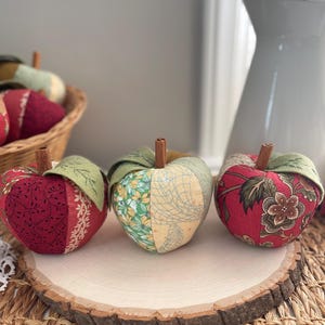 Red and green patchwork fabric apples displayed together on a natural wood slice for fall decor.