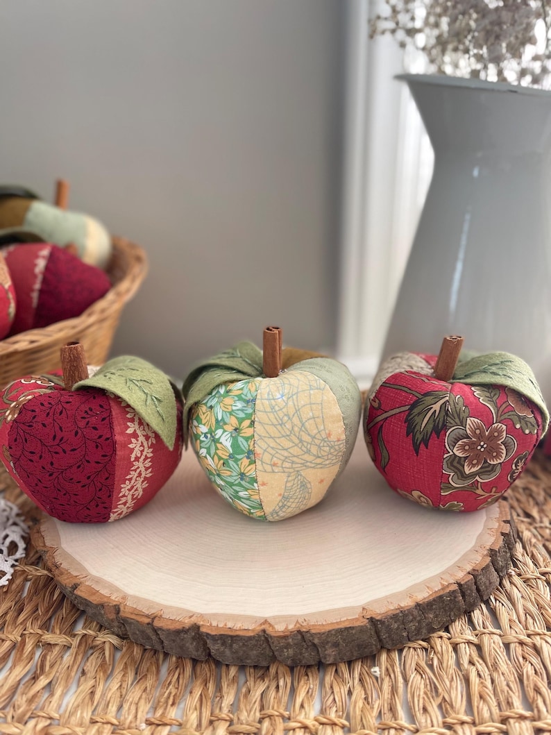 Red and green patchwork fabric apples displayed together on a natural wood slice for fall decor.