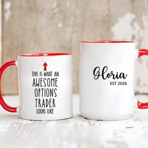 May include: Two white ceramic mugs with red handles and rims. One mug reads "THIS IS WHAT AN AWESOME OPTIONS TRADER LOOKS LIKE" with an arrow. The other mug says "Gloria EST 2026".