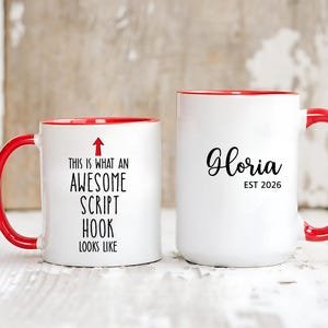 May include: Two white ceramic mugs with red handles and rims. One mug has the text "THIS IS WHAT AN AWESOME SCRIPT HOOK LOOKS LIKE" with an arrow. The other mug has the name "Gloria" and "EST 2026".
