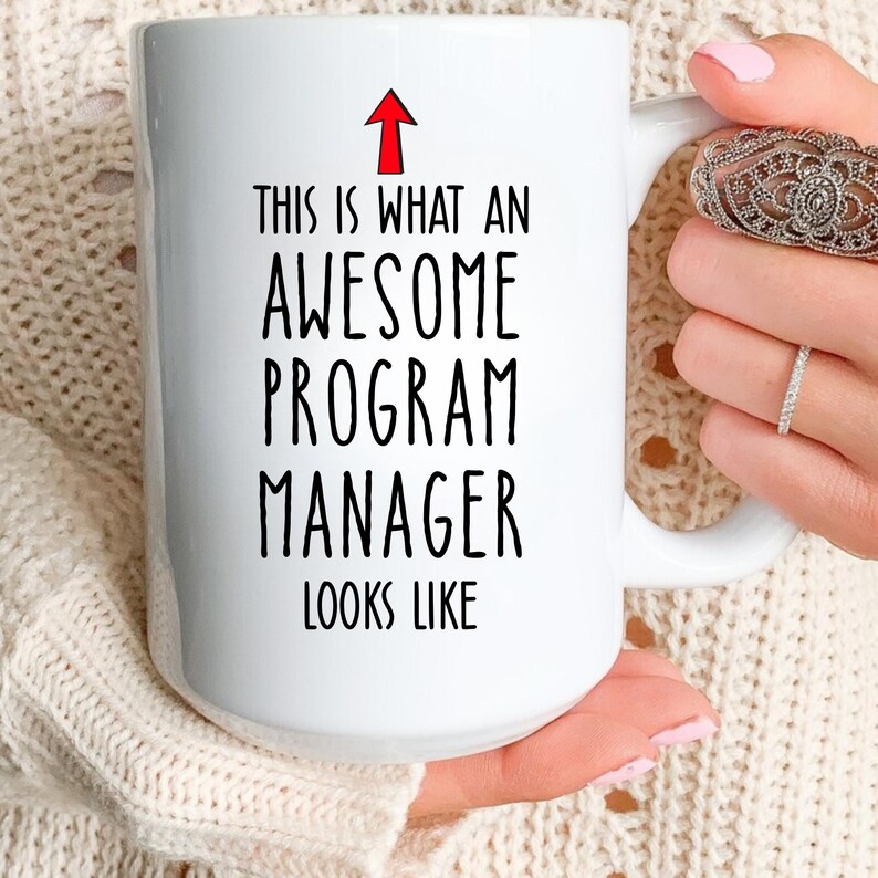 Puede incluir: Taza de cer&aacute;mica blanca con el texto "THIS IS WHAT AN AWESOME PROGRAM MANAGER LOOKS LIKE" en negro, con una flecha roja que apunta hacia arriba. La taza tiene un asa grande.