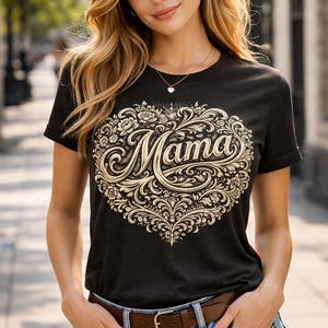 Puede incluir: Camiseta negra con un diseño de corazón decorativo color crema y la palabra "Mama" en una escritura adornada. La camiseta tiene mangas cortas y se combina con pantalones cortos de mezclilla azules y un cinturón marrón. La imagen muestra a una persona.