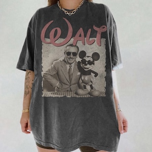 May include: Dark gray t-shirt featuring a vintage graphic of Walt Disney and Mickey Mouse wearing sunglasses. The word "Walt" is printed in pink script above the image. The shirt has a slightly faded, worn look.