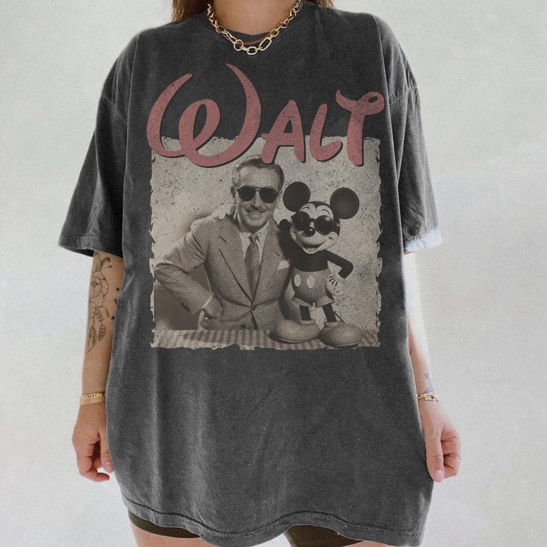 May include: Dark gray t-shirt featuring a vintage graphic of Walt Disney and Mickey Mouse wearing sunglasses. The word "Walt" is printed in pink script above the image. The shirt has a slightly faded, worn look.