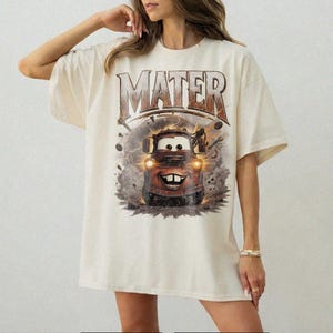 Puede incluir: Camiseta color crema con un gr&aacute;fico de Mate de la pel&iacute;cula Cars. El dise&ntilde;o incluye la palabra "MATER" encima del personaje, con una est&eacute;tica vintage y desgastada. La imagen muestra a Mate con rayos y herramientas.