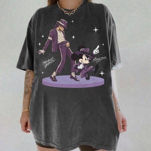 May include: Dark gray t-shirt featuring a graphic of Michael Jackson and Mickey Mouse in purple outfits. The design includes the text "Michael Jackson" and "Mickey Mouse" with star accents. The shirt has a vintage, washed look.