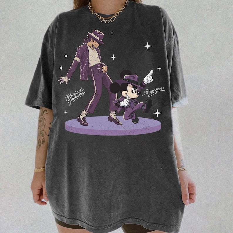May include: Dark gray t-shirt featuring a graphic of Michael Jackson and Mickey Mouse in purple outfits. The design includes the text "Michael Jackson" and "Mickey Mouse" with star accents. The shirt has a vintage, washed look.