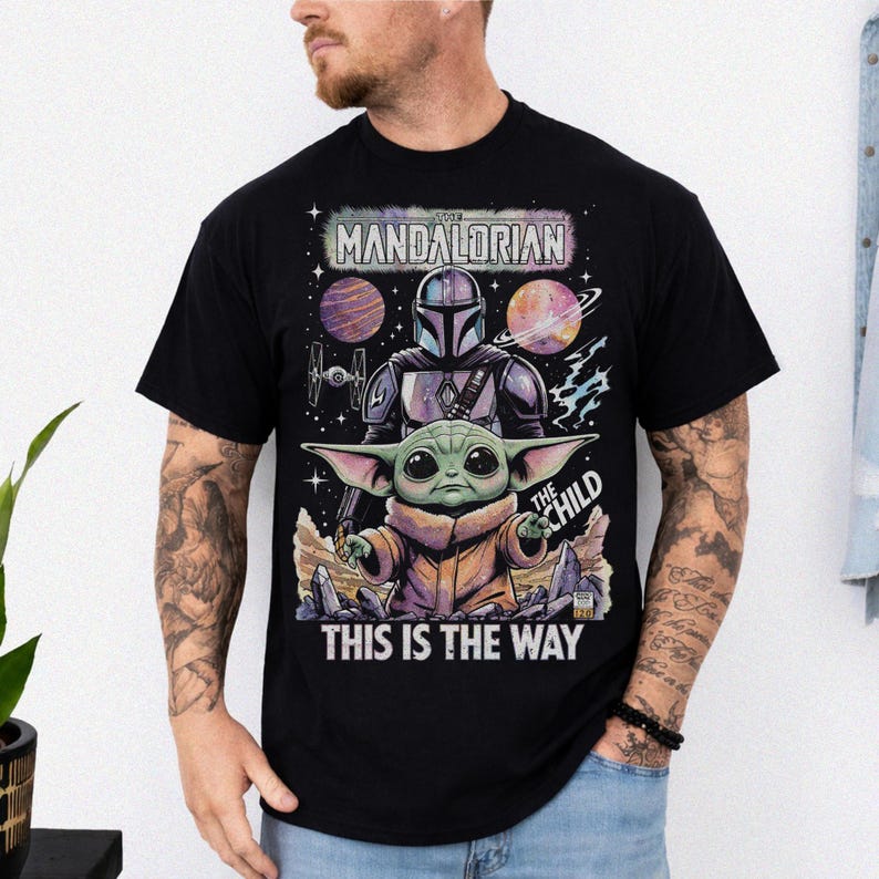 Pode incluir: Camiseta preta com um gr&aacute;fico de The Mandalorian e The Child, com o texto "THIS IS THE WAY". O design inclui uma cena espacial com planetas e uma nave espacial. O Mandaloriano &eacute; retratado em sua armadura.