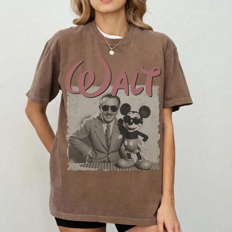 May include: Brown t-shirt featuring a vintage graphic of Walt Disney with Mickey Mouse. The graphic includes the name "Walt" in a pink script font. The image of Walt and Mickey is in black and white.