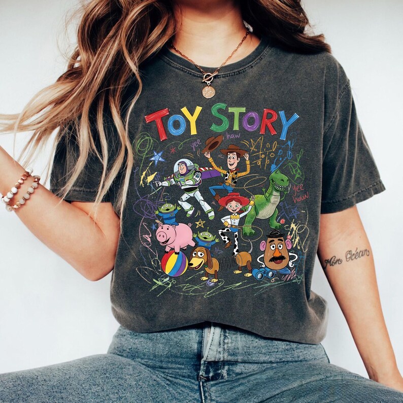 Puede incluir: Camiseta gris oscuro con un gr&aacute;fico colorido de los personajes de Toy Story. El dise&ntilde;o incluye a Buzz Lightyear, Woody y otros personajes de la pel&iacute;cula animada, con las palabras "TOY STORY" en una fuente l&uacute;dica.