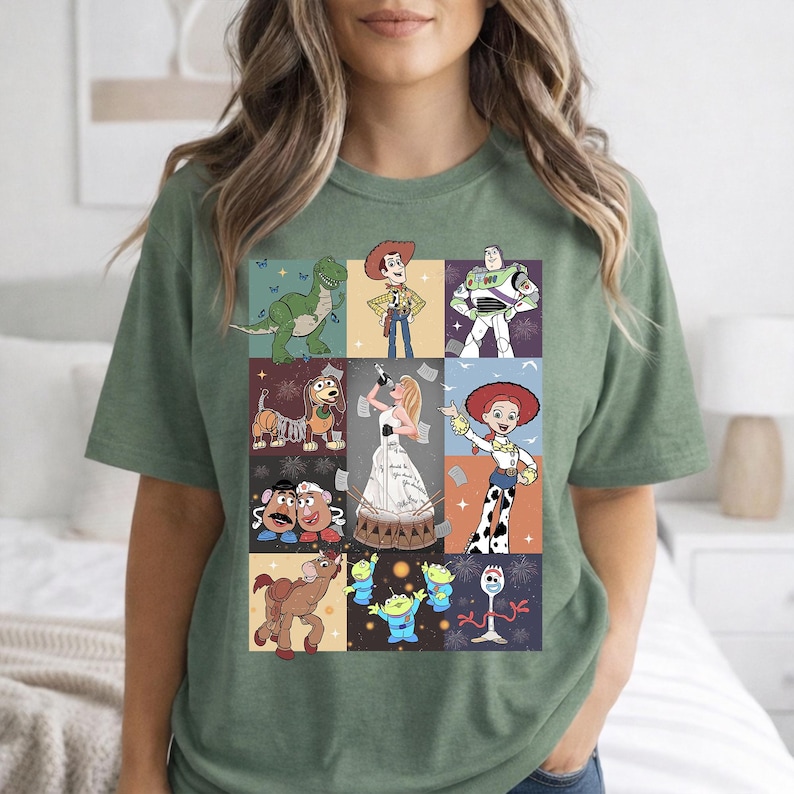 May include: A sage green short-sleeve t-shirt featuring a grid of nine rectangular panels. Each panel displays a different animated character from the Toy Story franchise, including Woody, Buzz Lightyear, Jessie, Rex, Slinky Dog, Mr. and Mrs. Potato Head, Bullseye, the Aliens, and Forky.