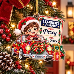 May include: A clear acrylic Christmas ornament featuring a cartoon character in a Santa hat driving a red car decorated with lights and a wreath. The car has a New Driver license plate and a sign reading Learner's Permit, Name: Percy, Date: 20xx.