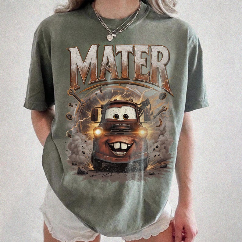 Puede incluir: Camiseta verde oliva con la palabra "MATER" en estilo vintage. El gr&aacute;fico presenta a Mater de la pel&iacute;cula Cars, con una cara sonriente y faros. El dise&ntilde;o incluye herramientas y rayos. La camiseta es de corte holgado.