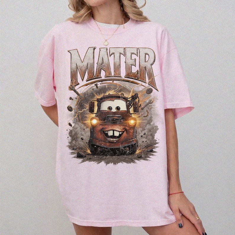 Puede incluir: Camiseta rosa claro con un dise&ntilde;o de Mate de la pel&iacute;cula Cars. La palabra "MATER" est&aacute; impresa encima del personaje en una fuente desgastada. El dise&ntilde;o incluye rayos y herramientas.