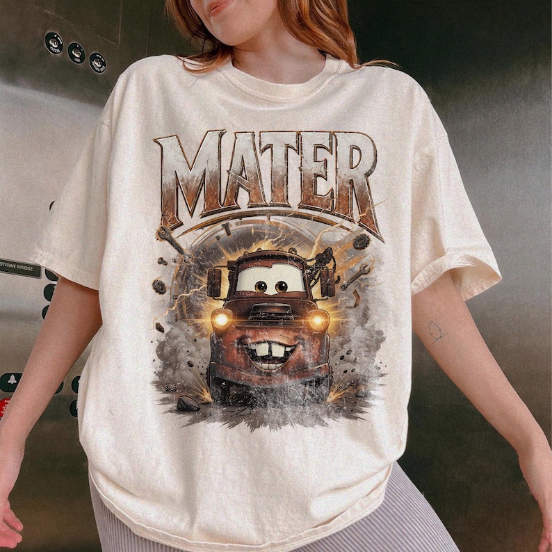Puede incluir: Camiseta color crema con un gr&aacute;fico de Mate de la pel&iacute;cula Cars. La palabra "MATER" est&aacute; impresa en la parte superior en una fuente marr&oacute;n desgastada. El gr&aacute;fico muestra a Mate con efectos de rayos y humo.