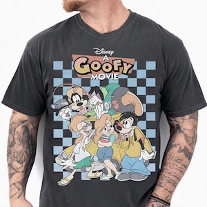 May include: Dark gray t-shirt featuring a graphic from Disney's "A Goofy Movie." The design includes the movie title and several cartoon characters against a blue and white checkered background. The shirt has a V-neck.