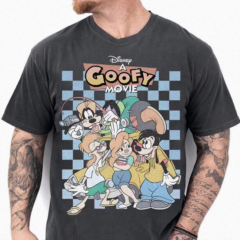 May include: Dark gray t-shirt featuring a graphic from Disney's "A Goofy Movie." The design includes the movie title and several cartoon characters against a blue and white checkered background. The shirt has a V-neck.