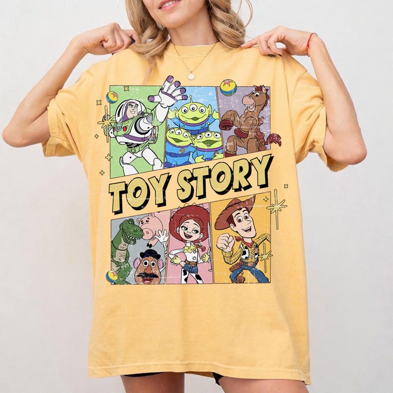 May include: Yellow t-shirt featuring a colorful graphic of characters from the animated movie "Toy Story." The design includes Buzz Lightyear, the aliens, Woody, and other characters. The words "TOY STORY" are printed in large, yellow letters.