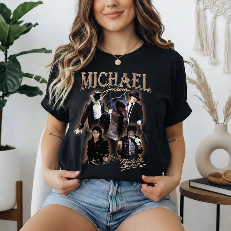 May include: Black t-shirt featuring a collage of images of Michael Jackson, with the name "MICHAEL" in gold lettering at the top. The design includes various poses of the singer, with his signature below.