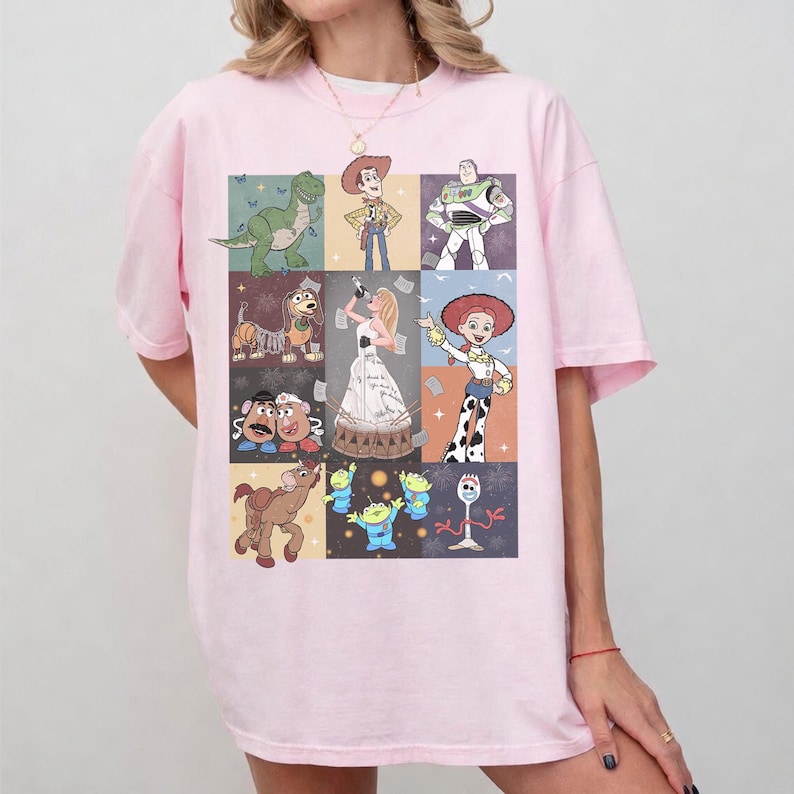 May include: A light pink short-sleeved t-shirt featuring a grid of various animated characters from the Toy Story franchise, including Woody, Buzz Lightyear, Jessie, Rex, Slinky Dog, Mr. and Mrs. Potato Head, Bullseye, the Aliens, and Forky.