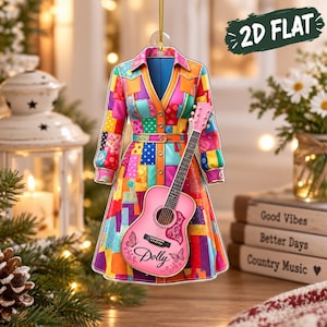 Könnte beinhalten: Ein flaches 2D-Hängeornament in Form eines langärmeligen Kleides mit buntem Patchwork-Muster in Rosa-, Blau-, Orange- und Gelbtönen. Eine rosa Akustikgitarre mit dem Namen Dolly und Schmetterlingsgrafiken ist über dem Kleid abgebildet.