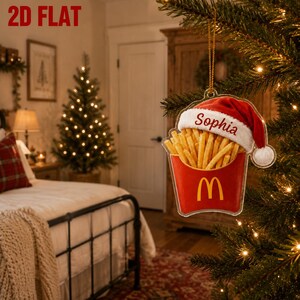 Könnte beinhalten: Ein flacher 2D-Weihnachtsbaumschmuck in Form einer roten Pommes-Frites-Schachtel. Die Pommes sind mit einer rot-weißen Weihnachtsmannmütze bedeckt, auf der der Name Sophia in roter Schrift steht. Die rote Schachtel zeigt ein gelbes M-Logo.