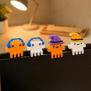 May include: Four pixel-art style figures perched on a monitor edge. Two are orange and white ghosts wearing blue headphones, one is an orange ghost wearing a purple wizard hat, and one is a white ghost wearing a yellow wizard hat with black trim.