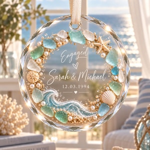 K&ouml;nnte beinhalten: Ein kreisf&ouml;rmiges Glasornament mit facettiertem Rand, verziert mit Meerglas, Perlen, einem Seestern und einer Muschel. Der Text lautet Engaged, Sarah & Michael, 12.03.1994, erg&auml;nzt durch eine Wellenillustration im unteren Bereich.