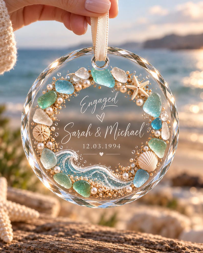 K&ouml;nnte beinhalten: Ein rundes, facettiertes Glasornament mit einem Kranzdesign im Strandthema. Es enth&auml;lt Meerglas, kleine Perlen, Sand, einen Seestern und eine Muschel. Der Text lautet Engaged, Sarah & Michael und 12.03.1994, mit einer blauen Welle.