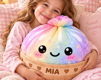 May include: A plush toy shaped like a rainbow-colored dumpling with a smiling face, stars, and pink cheeks, nestled inside a light-colored wooden steamer basket. The basket is engraved with the name MIA and small heart symbols.