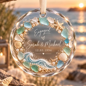 K&ouml;nnte beinhalten: Ein kreisf&ouml;rmiges Glasornament mit einem Strand-Themenkranz aus Meerglas, Perlen, einem Seestern und einer Muschel. In der Mitte steht Engaged, Sarah & Michael, 12.03.1994, mit einer gemalten blauen Welle am unteren Rand, aufgeh&auml;ngt an einem Band.