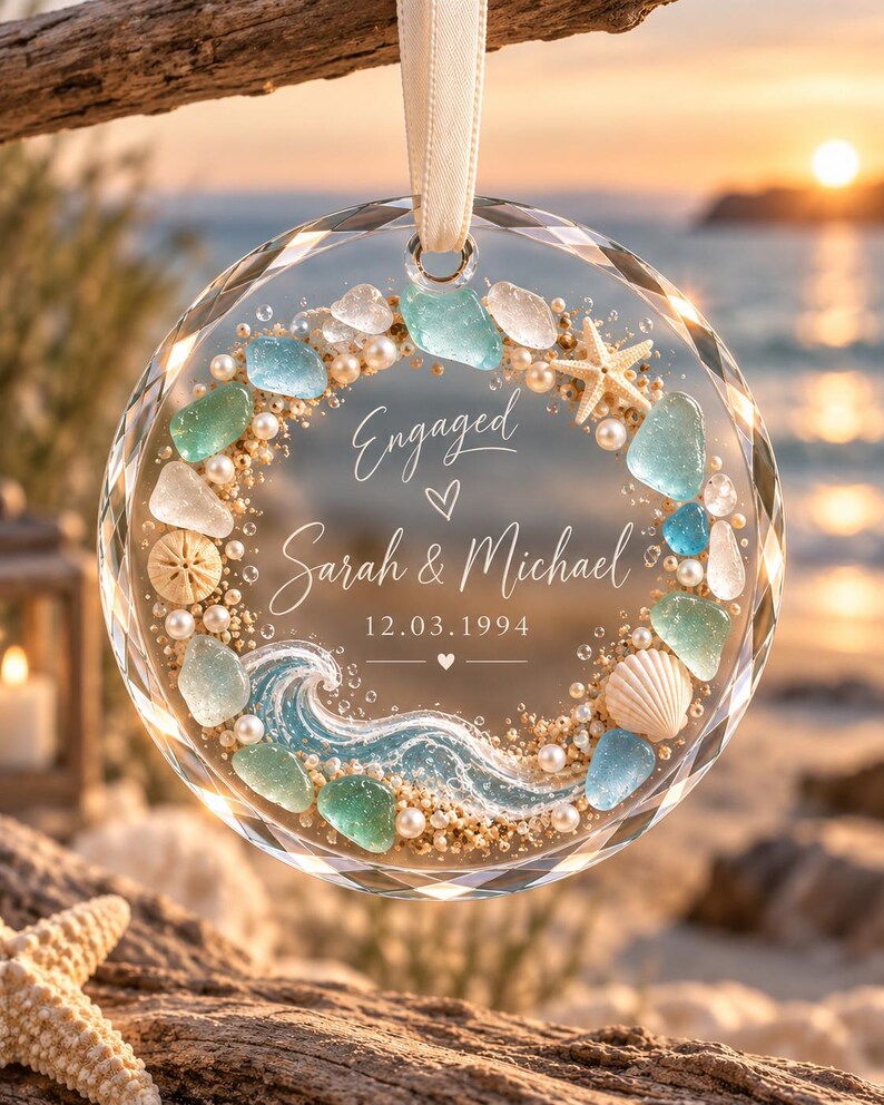 K&ouml;nnte beinhalten: Ein kreisf&ouml;rmiges Glasornament mit einem Strand-Themenkranz aus Meerglas, Perlen, einem Seestern und einer Muschel. In der Mitte steht Engaged, Sarah & Michael, 12.03.1994, mit einer gemalten blauen Welle am unteren Rand, aufgeh&auml;ngt an einem Band.