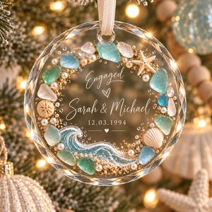 K&ouml;nnte beinhalten: Ein kreisf&ouml;rmiges Ornament aus klarem Glas mit facettiertem Rand, verziert mit einem Kranz aus Meerglas, Perlen, Sand, einem Seestern und einer Muschel. Die Mitte zeigt den Text Engaged, Sarah & Michael, 12.03.1994 und eine blaue Meereswelle.