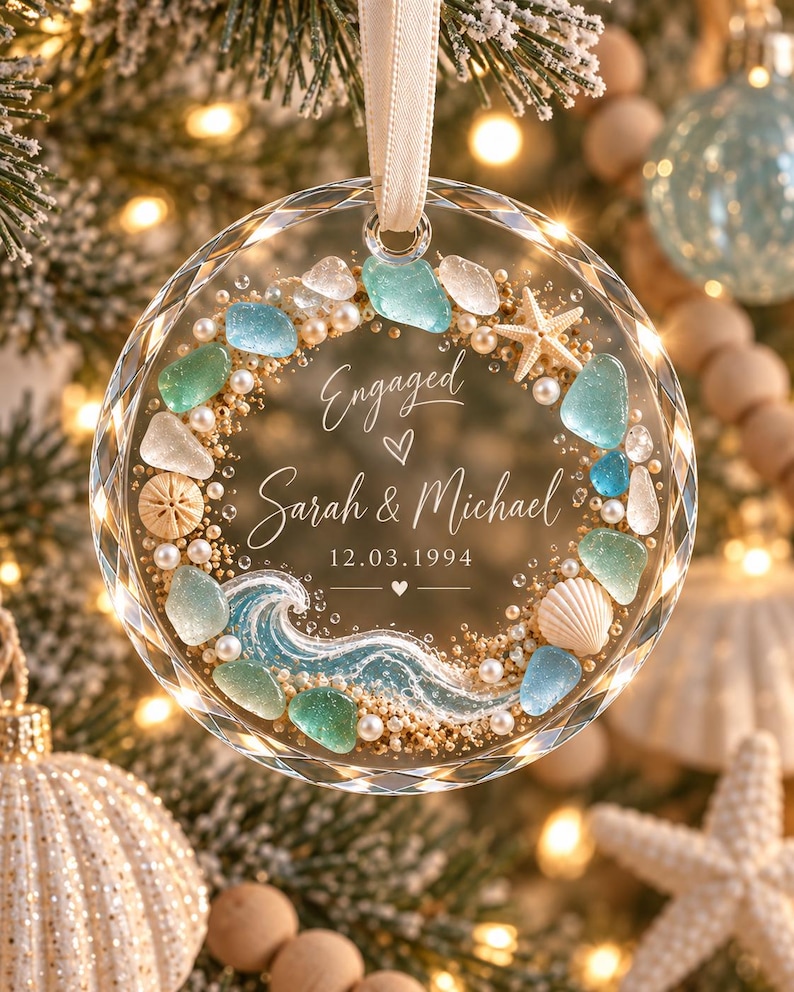K&ouml;nnte beinhalten: Ein kreisf&ouml;rmiges Ornament aus klarem Glas mit facettiertem Rand, verziert mit einem Kranz aus Meerglas, Perlen, Sand, einem Seestern und einer Muschel. Die Mitte zeigt den Text Engaged, Sarah & Michael, 12.03.1994 und eine blaue Meereswelle.