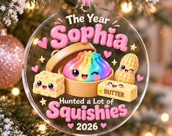 Könnte beinhalten: Ein runder, transparenter Anhänger mit dem Text The Year Sophia Hunted a Lot of Squishies 2026. Das Motiv zeigt einen regenbogenfarbenen Teigkloß im Bambusdämpfer, ein Stück Käse, eine Erdnuss und ein Stück Butter, alle mit aufgedruckten Gesichtern.