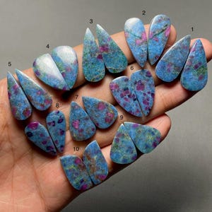 May include: A collection of ten pairs of polished, teardrop-shaped gemstones featuring a mottled blue and green matrix with embedded vibrant pink and magenta inclusions. Each pair is numbered from one to ten, showcasing a smooth, flat surface.