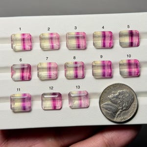 May include: Thirteen rectangular gemstones with a mix of clear, yellow, and pink hues are displayed. A US nickel coin is next to the gemstones for size comparison. The gemstones are numbered 1 through 13.