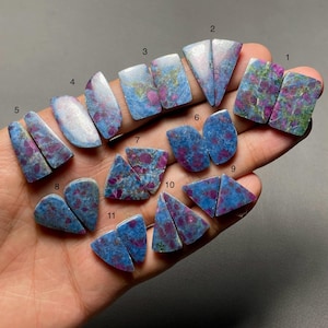 May include: A collection of eleven pairs of polished, flat-backed gemstones featuring a vibrant mix of blue and magenta-pink mineral inclusions. Each pair is numbered from 1 to 11, showcasing varied geometric shapes including triangles, rectangles, and teardrops with distinct colour patterns.