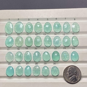 Peut inclure: Une collection de 30 cabochons de pierres pr&eacute;cieuses bleu clair, chacun avec une forme et une taille uniques, dispos&eacute;s en rang&eacute;es. Une pi&egrave;ce de monnaie est incluse pour la comparaison des tailles. Les pierres pr&eacute;cieuses varient en clart&eacute; et en facettage.