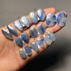 May include: Nine blue sapphire gemstones in diverse shapes, including oval, pear, and marquise cuts. The faceted sapphires display a range of blue hues with some inclusions. Each stone is presented on a white tag.