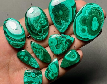 May include: Ten polished malachite gemstones in various shapes and sizes, each featuring distinct green concentric banding and swirling patterns. The stones are numbered one through ten, displaying smooth, reflective surfaces and vibrant green hues.